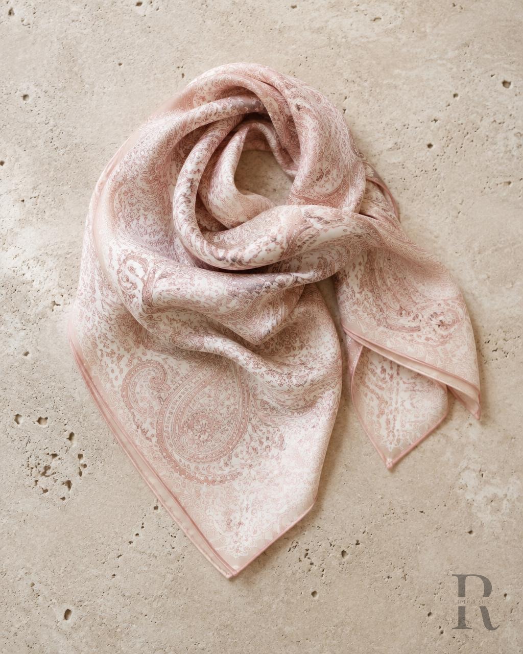 Bufanda con estampado paisley en rosa blush doblada sobre piedra